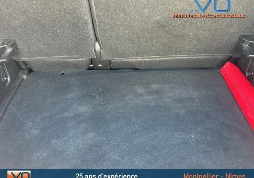 Coffre spacieux du Renault Captur gris TCe 90 Business 2022, avec tapis noir et triangle de sécurité rouge sur le côté droit.