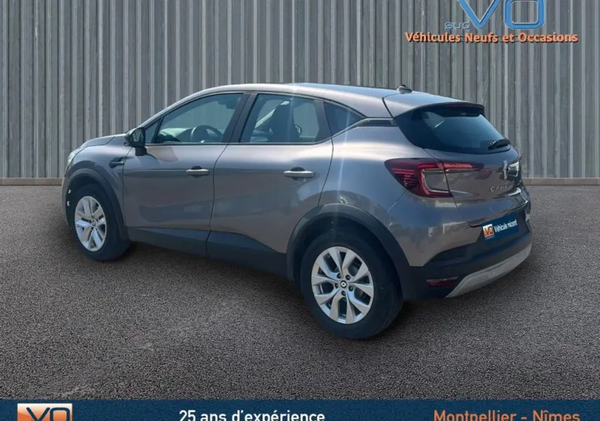 Renault Captur TCe 90 Business gris en 3/4 arrière droit, stationné devant un mur métallique.