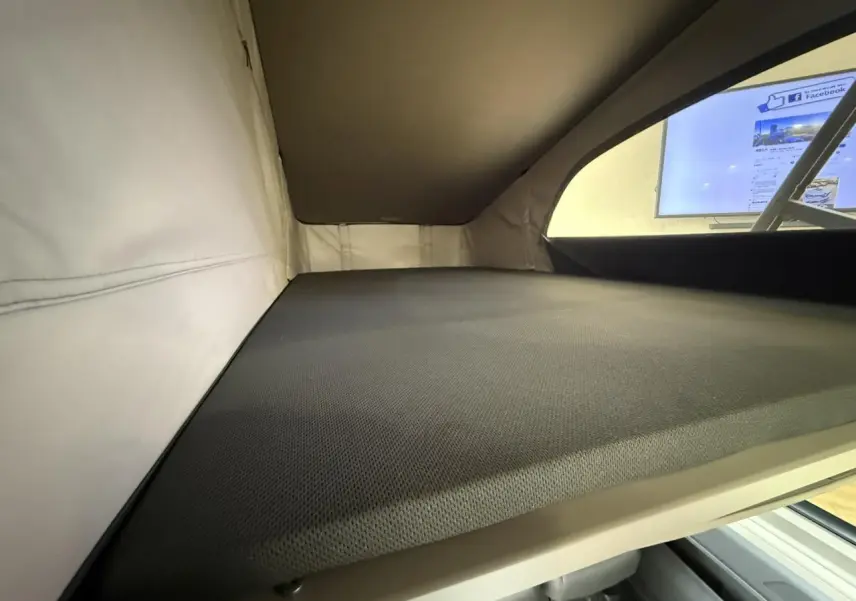 Vue intérieure du couchage supérieur du Volkswagen California T7 2024 avec toit relevable et matelas gris.