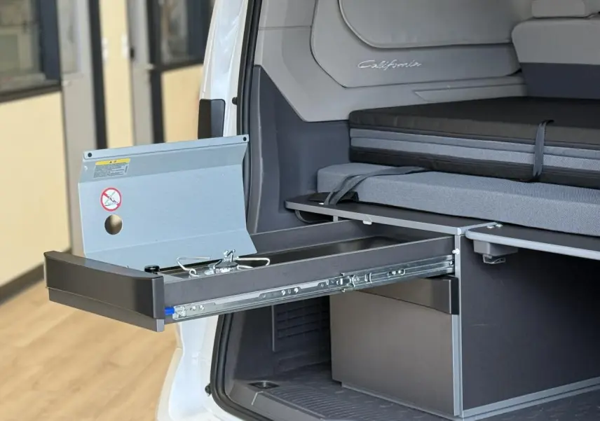 Vue arrière droite du Volkswagen California blanc Candy montrant la mini-cuisine coulissante et la banquette intérieure.