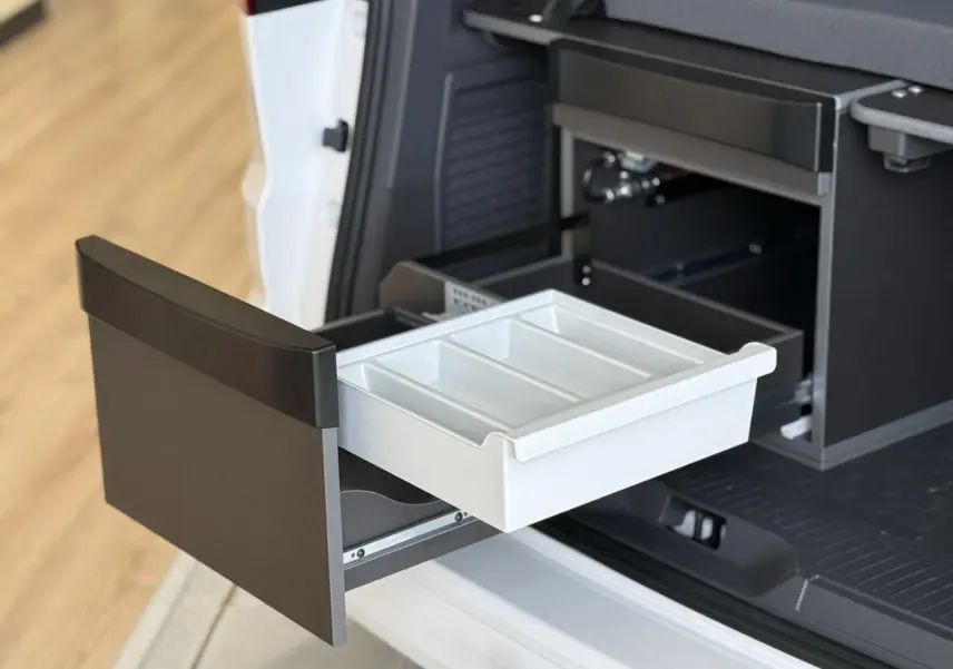 Tiroir de rangement ouvert à l'arrière côté droit du Volkswagen California T7 blanc, montrant la cuisine intégrée.