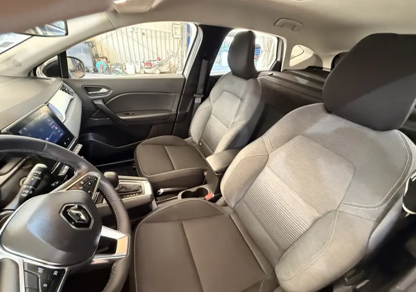 Vue intérieure côté conducteur du Renault Captur blanc 2021, avec sièges bicolores gris et noir et tableau de bord moderne.