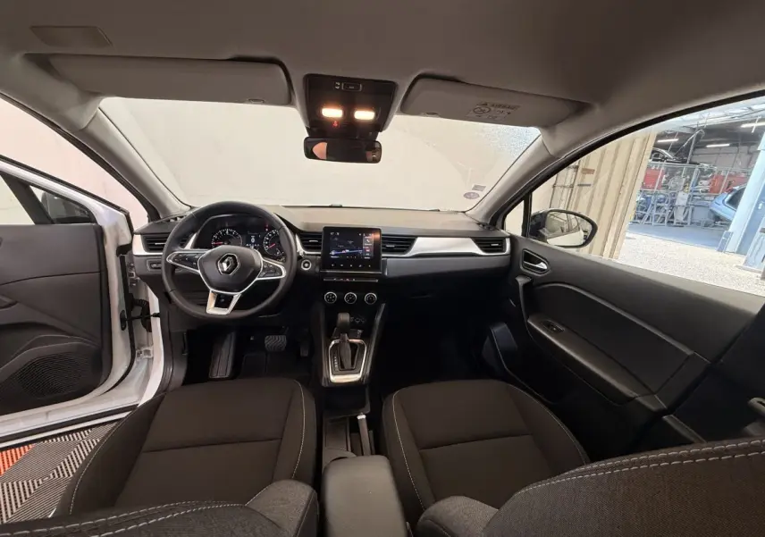Vue intérieure avant du Renault Captur blanc 2021, montrant le tableau de bord avec écran tactile central et volant multifonctions.