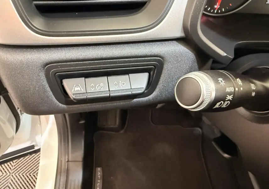 Vue intérieure côté gauche du tableau de bord du Renault Captur blanc, avec commandes d'assistance à la conduite et commodo des phares.