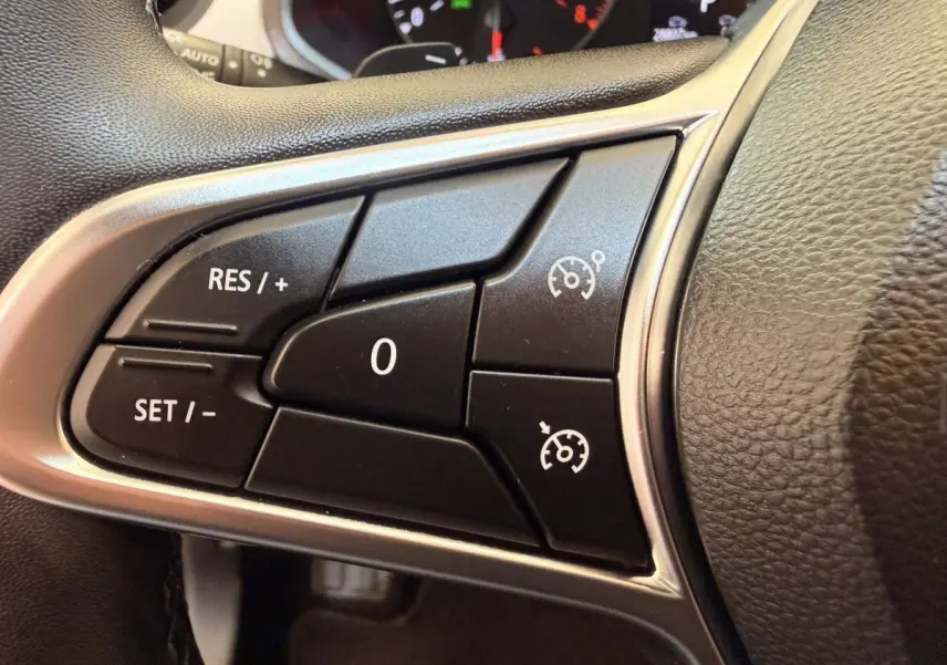 Gros plan sur les commandes de régulateur de vitesse à gauche du volant en cuir noir du Renault Captur blanc 2021.