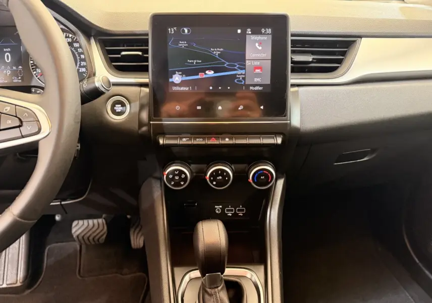 Vue intérieure centrée sur la console centrale et écran tactile du Renault Captur blanc, avec commandes climatisation et levier de boîte auto.