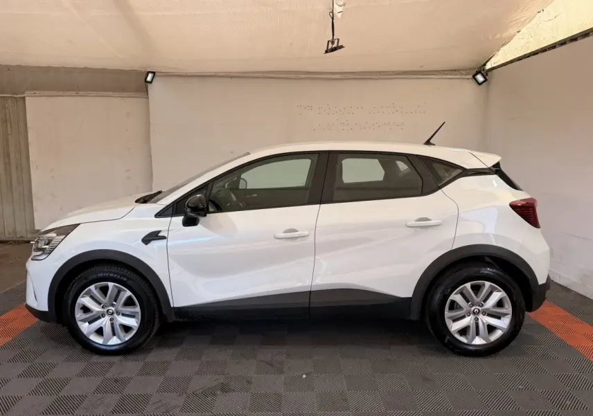 Profil côté gauche d’un Renault Captur blanc 2021 avec jantes alliage et rétroviseurs noirs dans un garage.