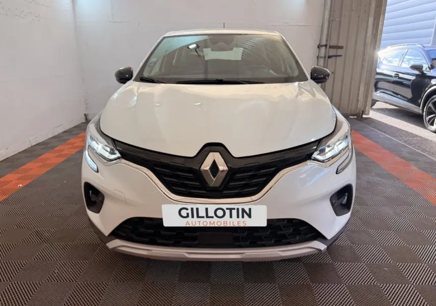 Vue avant d'un Renault Captur blanc 2021 dans un garage avec calandre noire et feux LED allumés.