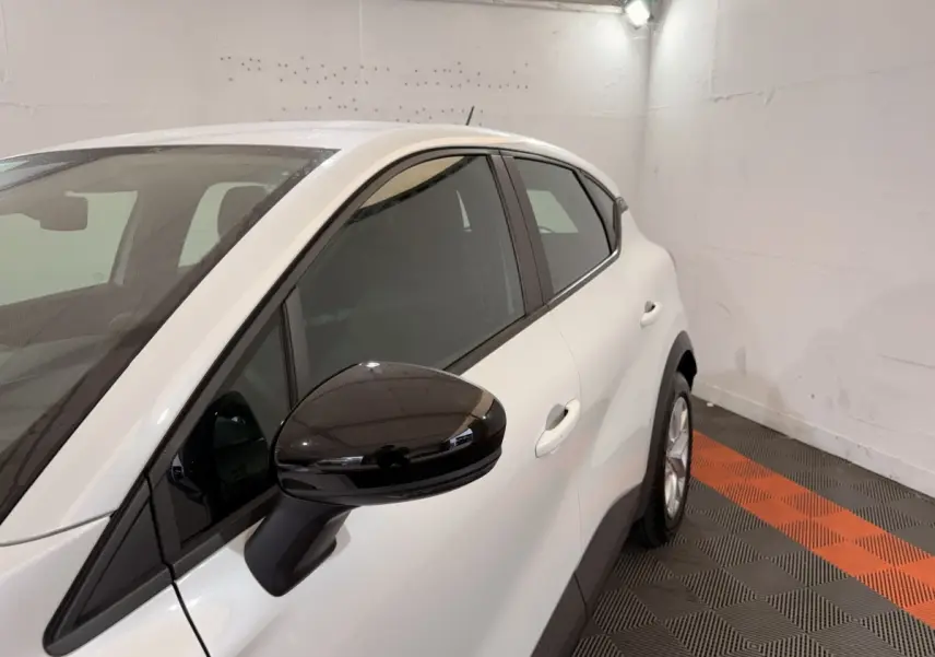 Vue de côté droit avant d’un Renault Captur blanc avec rétroviseur noir brillant dans un garage.