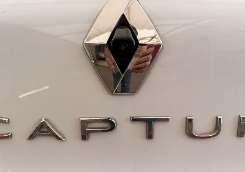 Gros plan sur le logo Renault avec caméra intégrée et lettrage CAPTUR sur la carrosserie blanche du véhicule.