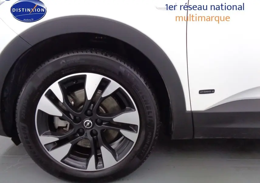 Gros plan sur la roue avant gauche du SUV Opel Grandland X blanc nacré avec badge Hybrid 4 sur la carrosserie.