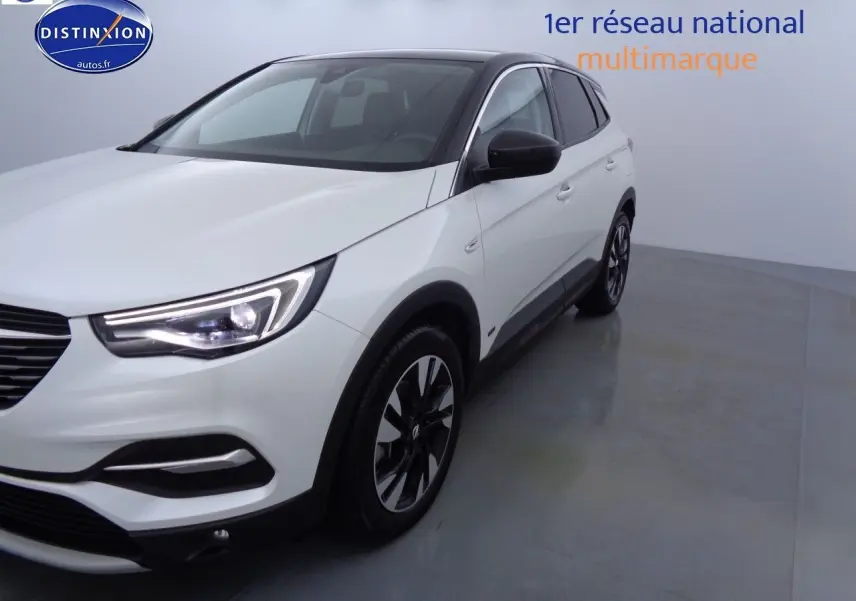 Opel Grandland X blanc nacré, vue 3/4 avant droit, avec jantes alliage noires et phares LED allumés.