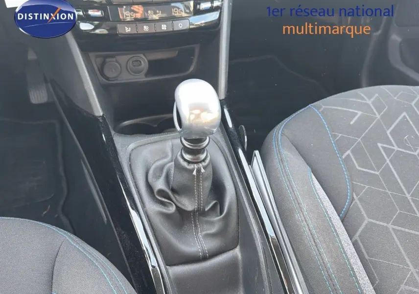 Gros plan sur la console centrale et levier de vitesse manuel d'une Peugeot 2008 gris platinium, sièges tissu noir avec surpiqûres bleues.