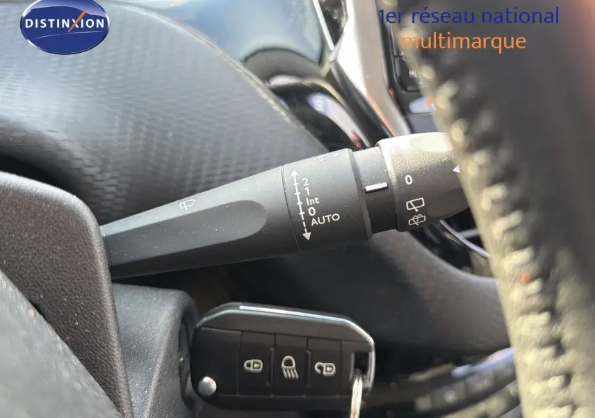 Gros plan sur la commande d'essuie-glace et la clé de contact d'une Peugeot 2008 gris platinium, intérieur noir.