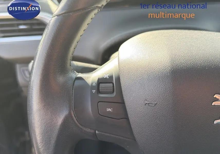 Gros plan sur le volant en cuir noir du Peugeot 2008 gris platinium, montrant les commandes audio intégrées.