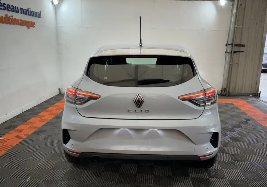 Vue arrière d'une Renault Clio gris clair 2025 avec feux LED allumés dans un garage éclairé.