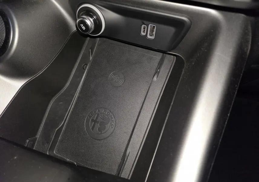 Gros plan sur la console centrale noire de l'Alfa Romeo Tonale 2023 avec zone de recharge sans fil et ports USB.