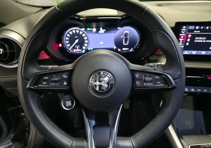 Vue rapprochée du volant en cuir noir de l'Alfa Romeo Tonale 2023 avec tableau de bord digital et bouton start/stop.