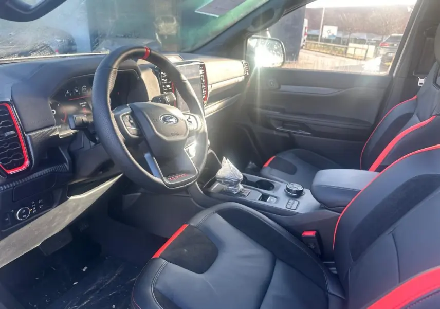 Vue intérieure côté conducteur du Ford Ranger Raptor 2025, sièges noirs avec surpiqûres rouges et tableau de bord moderne.