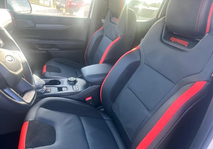 Vue intérieure côté conducteur du Ford Ranger Raptor 2025, sièges noirs avec surpiqûres rouges et logo Raptor brodé.