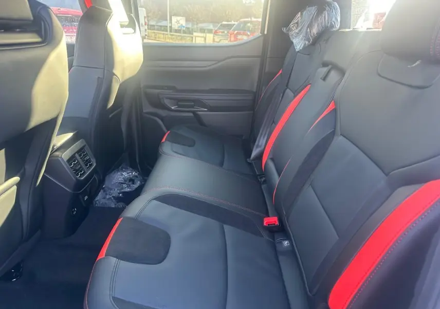 Vue latérale intérieure arrière du Ford Ranger 2025, sièges en cuir noir avec surpiqûres et inserts rouges.