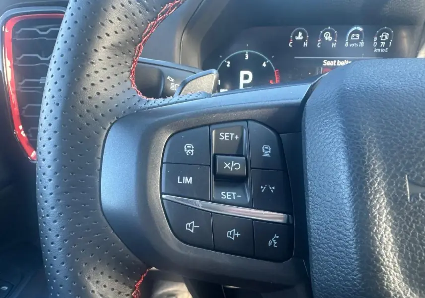 Gros plan sur le volant noir perforé avec surpiqûres rouges du Ford Ranger 2025, montrant les commandes multifonctions à gauche.