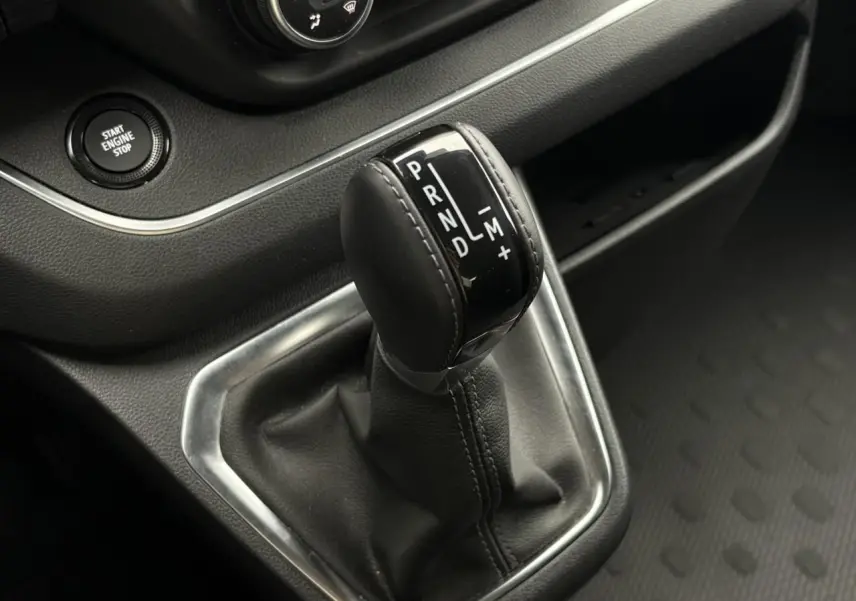 Gros plan sur le levier de vitesses automatique noir du Nissan Primastar gris, avec bouton start engine stop visible.