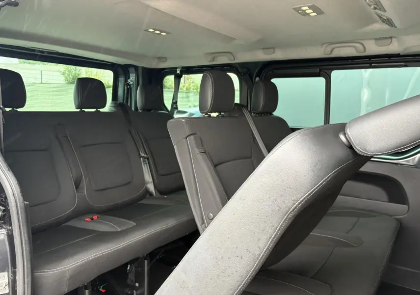 Vue intérieure côté droit du Nissan Primastar gris Comète montrant les sièges amovibles en tissu noir sur trois rangées.