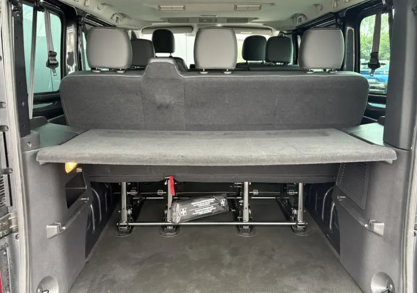 Vue arrière du coffre ouvert du Nissan Primastar gris, montrant la banquette arrière et la tablette de séparation.