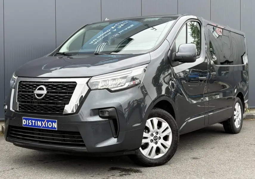 Nissan Primastar gris Comète en 3/4 avant droit, avec hayon vitré et jantes alliage 17 pouces visibles.