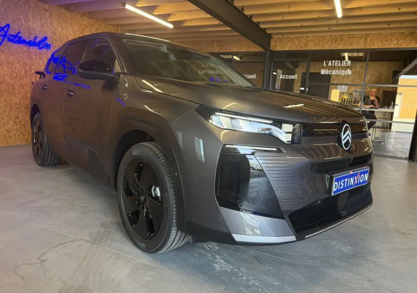 Vue 3/4 avant droit d'un Citroën C5 Aircross gris 2026 avec jantes noires et calandre distinctive en intérieur d'atelier.