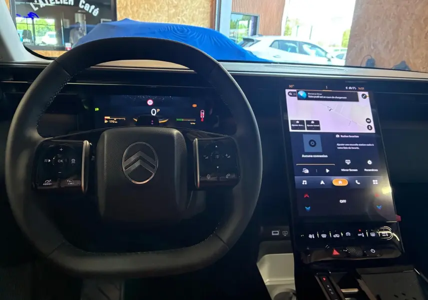 Vue intérieure centrée sur le volant noir et l’écran tactile vertical du tableau de bord du Citroën C5 Aircross gris hybride.