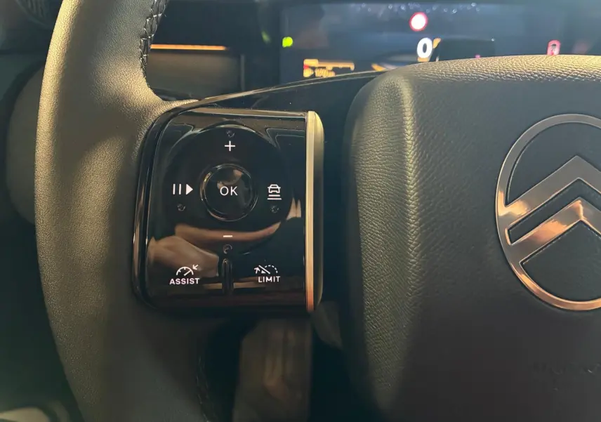 Gros plan sur la partie gauche du volant gris du Citroën C5 Aircross 1.2 Hybride 145 Plus avec commandes intégrées et logo Citroën visible.