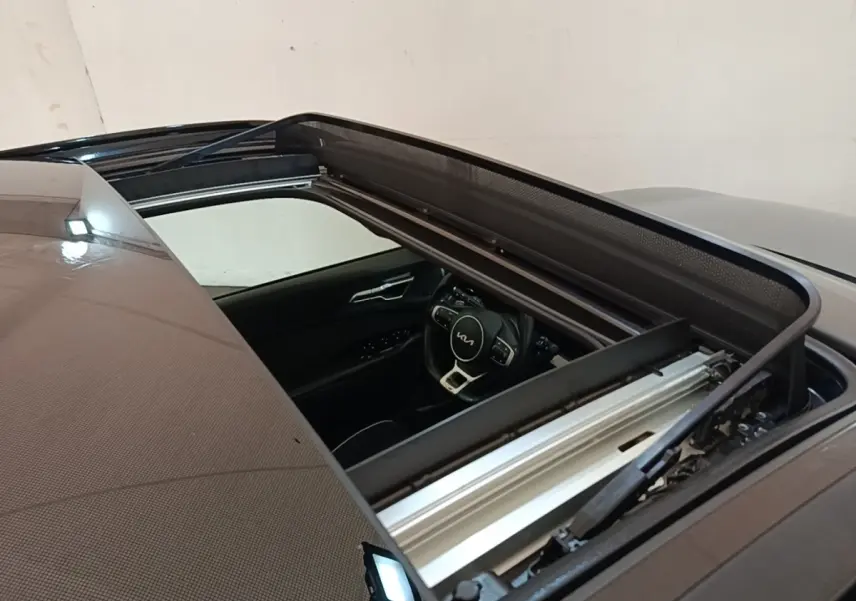 Vue plongeante sur le toit ouvrant ouvert d’un Kia Sportage gris clair, avec aperçu du volant et intérieur noir.