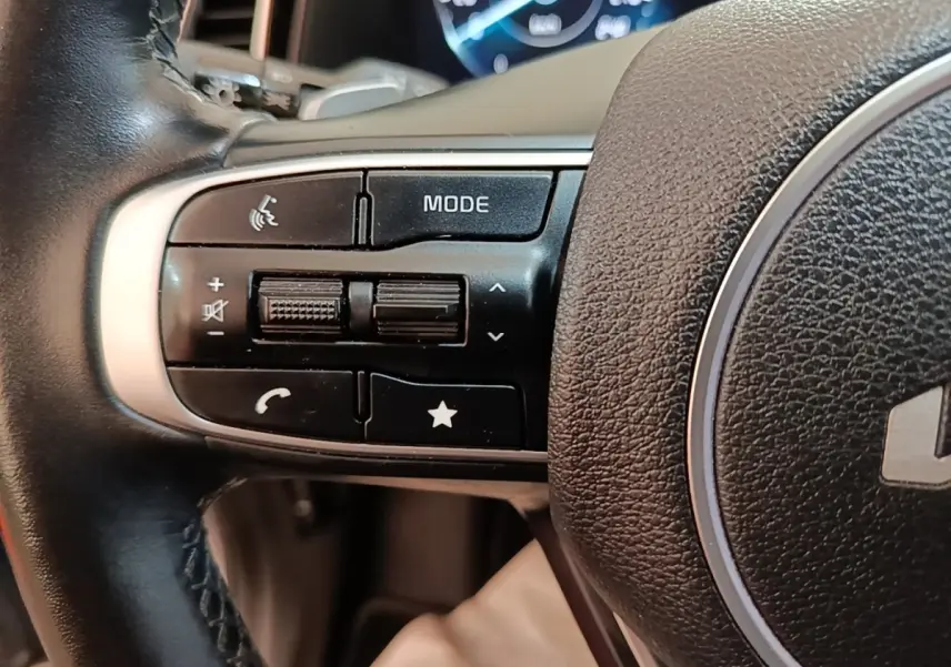 Gros plan sur les commandes gauche du volant cuir du Kia Sportage gris clair 2022 avec affichage numérique en arrière-plan.