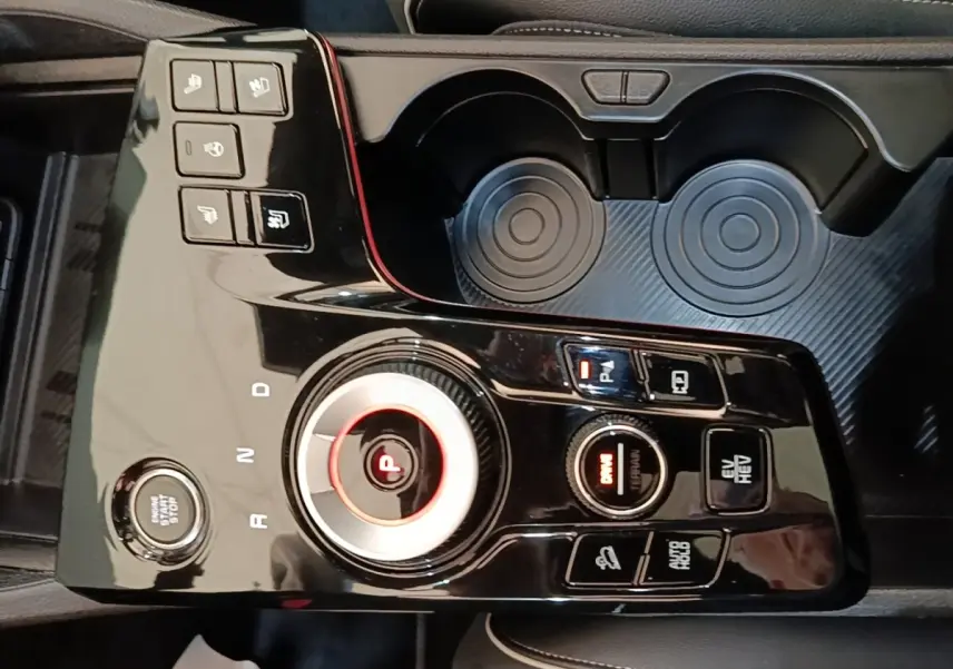 Vue plongeante sur la console centrale noire brillante du Kia Sportage hybride rechargeable avec molette de sélection de vitesse et boutons multifonctions.