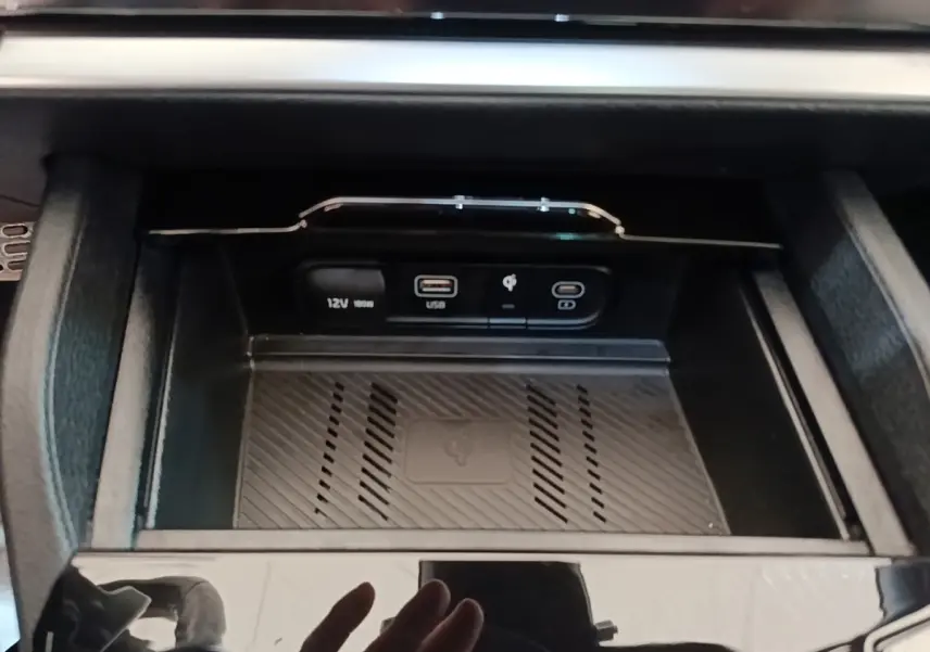 Gros plan sur la console centrale du Kia Sportage gris clair, montrant prises USB, 12V et charge sans fil.