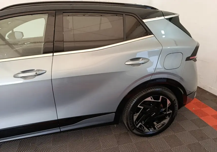 Vue latérale droite du Kia Sportage gris clair hybride rechargeable, mettant en valeur la porte arrière et la roue au design moderne.