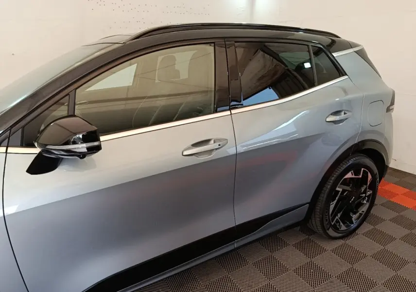 Vue latérale côté gauche d'un KIA Sportage gris clair avec toit noir et jantes noires design.