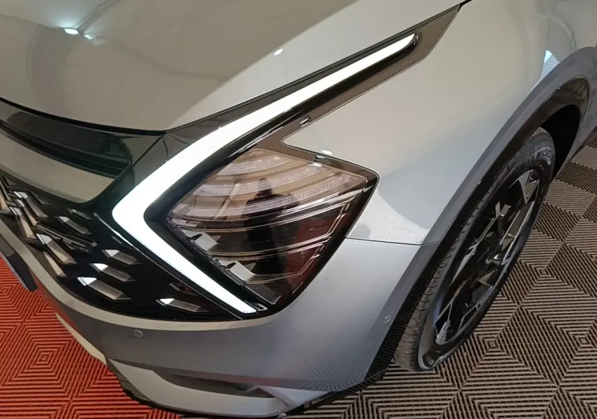 Gros plan sur l'avant droit gris clair du KIA SPORTAGE 2022 avec phare LED en forme de boomerang et jante noire.