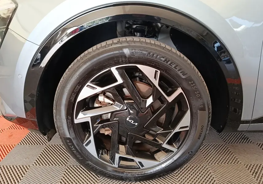 Gros plan sur la roue avant droite du KIA Sportage gris clair, jante alliage noire et argentée au design moderne.