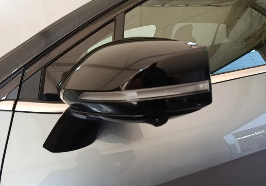 Rétroviseur noir en gros plan côté gauche d’un KIA SPORTAGE gris clair avec fenêtre arrière visible en arrière-plan.
