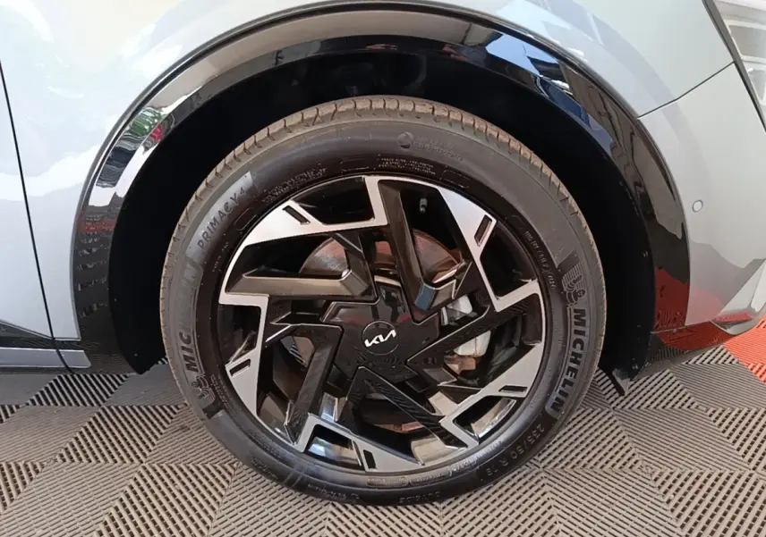 Gros plan sur la roue avant gauche du KIA Sportage gris clair, mettant en valeur la jante noire et argentée au design géométrique.