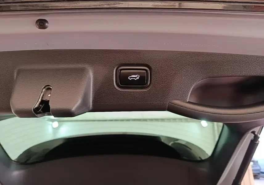Bouton d'ouverture électrique du coffre sur la partie intérieure du hayon d'un KIA Sportage gris clair.