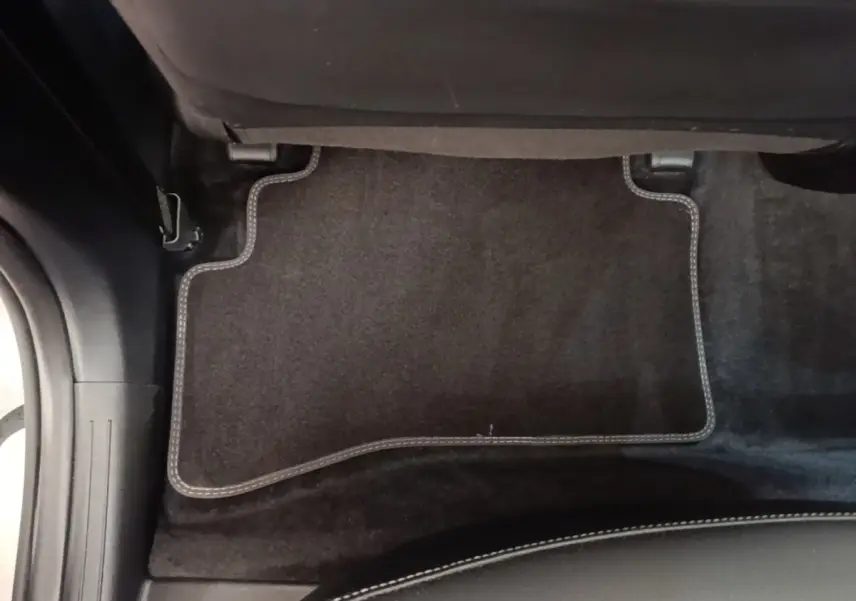 Détail du tapis de sol noir avec surpiqûres blanches sous le siège arrière du Kia Sportage gris clair 2022 hybride rechargeable.