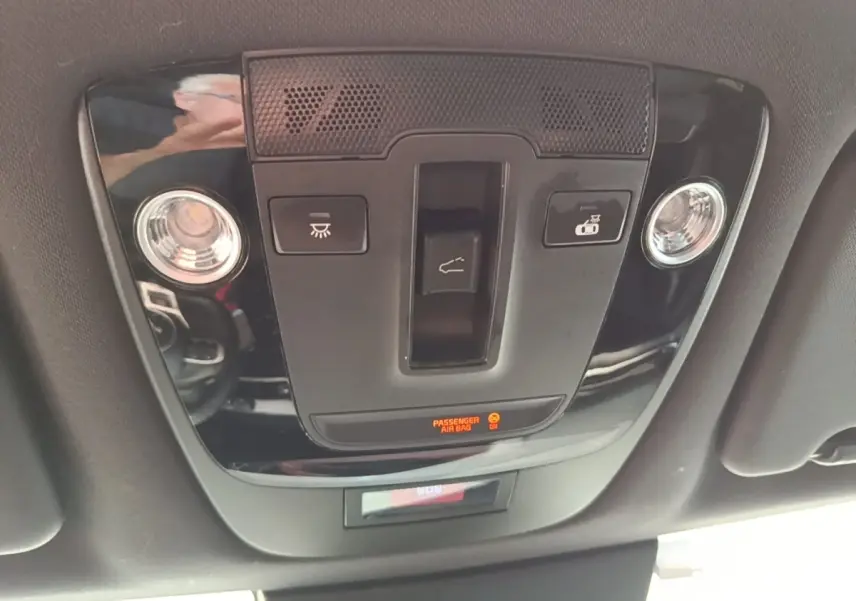 Vue rapprochée du panneau de commande de toit noir brillant avec éclairage et indicateur airbag passager actif dans un Kia Sportage gris clair 2022.