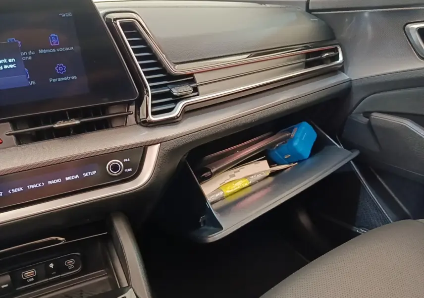 Intérieur du Kia Sportage 2022, vue côté passager sur la boîte à gants ouverte et tableau de bord moderne noir.