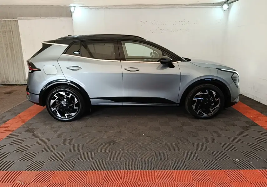 Vue de profil côté gauche d'un KIA Sportage gris clair avec toit noir et jantes noires design moderne dans un garage.