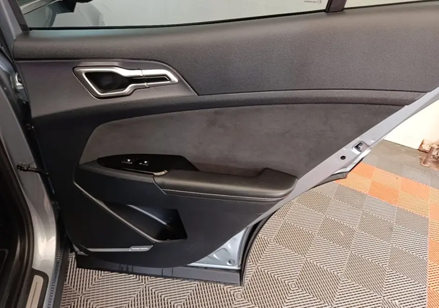 Vue intérieure côté gauche de la porte arrière grise claire du Kia Sportage avec garniture noire et commandes de fenêtre.
