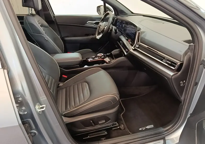 Intérieur avant droit du KIA Sportage gris clair 2022, sièges cuir noirs et tableau de bord digital large.
